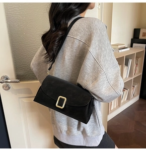 Détail du sac à bandoulière en daim noir mat avec boucle dorée porté par un modèle