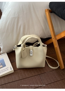 Close-up of cream-colored litchi-grain leather bucket bag with silver metal twist lock