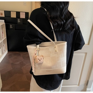 Chic cream canvas tote bag with leather trim and plush bear charm shown on model