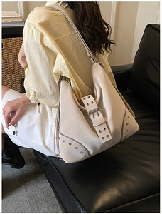 Close-up of cream leather hobo bag with silver rivets and metal buckle detail