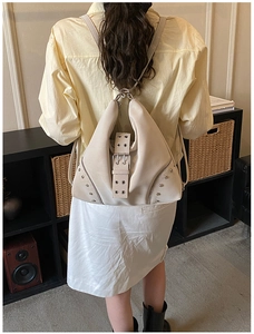 Detailed back view of a beige PU leather backpack with rivets and metal buckles worn by a model