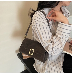 Détail du sac à bandoulière vintage marron foncé avec grande boucle dorée sur daim texturé