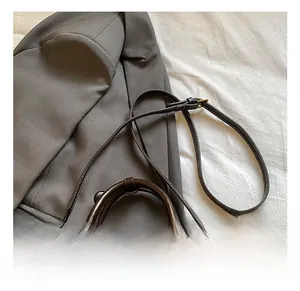 Detail einer braunen Boston-Tasche aus Leder mit goldenen Elementen auf grauem Blazer