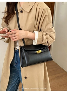 Détail d'un sac bandoulière vintage en cuir noir avec boucle dorée porté sur un trench-coat
