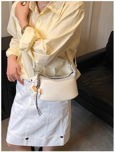Close-up of white half-moon shoulder bag with glossy crinkle texture and horse charm