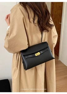 Détail d'un sac vintage en cuir noir avec fermoir tournant doré sur un trench-coat