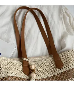 Detail of straw tote bag with brown leather strap, wooden beads and zipper closure