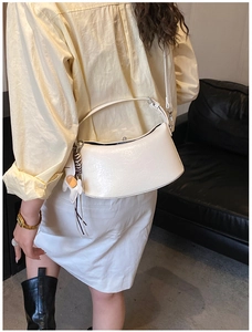 Detailed side view of white crescent bag with puppy charm and metallic buckle on leather sofa