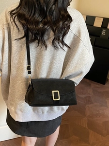 Sac bandoulière noir mat minimaliste avec boucle dorée porté par un mannequin