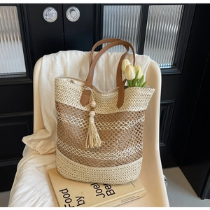 Close-up of woven straw tote bag with brown leather handles and wooden bead tassels