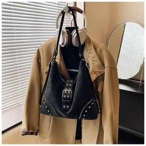 Close-up of black rivet tote bag with silver buckles and studs against a trench coat