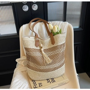 Detail of handwoven straw beach bag with striped texture, leather handle and tassel charm