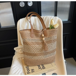 Close-up of woven straw tote bag featuring long tassel decor and leather handles