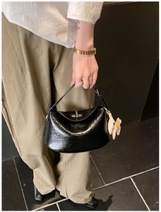Detail of black glossy croissant bag featuring silver turn-lock and cute floral charm