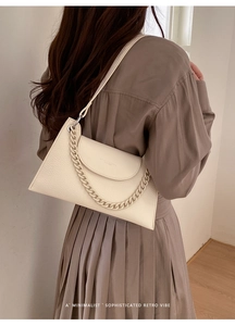 Detail of a creamy white leather trapezoid bag with chain decor and a curved flap cover