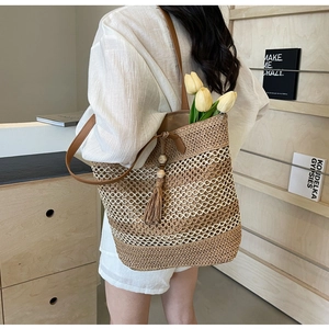 Detail of a large straw tote bag with wave pattern, wooden bead tassel and brown shoulder strap