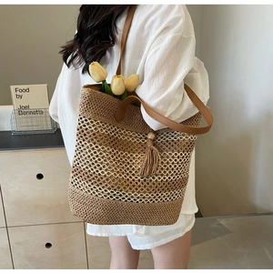 Detail of hand-woven straw tote bag with mesh hollow design and brown leather tassel