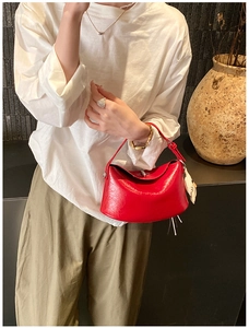 Detail of red leather crossbody bag with white cat charm and shoulder strap