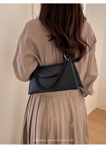 Detail view of black pebble leather underarm bag with thick chain strap on model