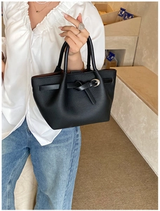 Détail du sac à main en cuir grainé noir avec nœud décoratif et boucles métalliques