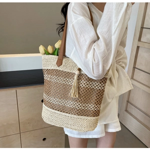 Detail of large straw tote bag with beige tassels and brown leather straps for beach holidays