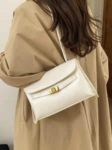 Sac bandoulière minimaliste en cuir blanc crème avec fermoir doré sur un trench-coat kaki