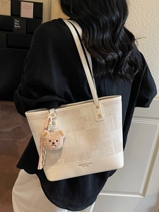 Chic beige canvas tote bag with leather trim and bear pendant worn by a model