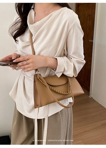 Detail showing textured camel leather crossbody bag with bold golden chain decoration