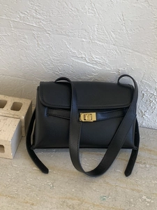 Sac bandoulière minimaliste en cuir noir avec boucle dorée posé sur une surface en pierre