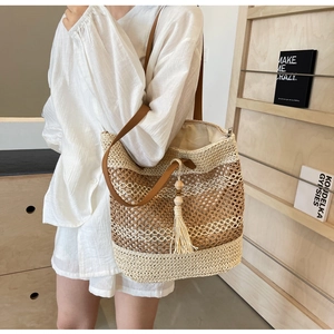 Detail of straw tote bag with brown leather straps and tassels in a lifestyle setting
