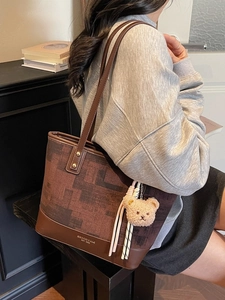 Large dark brown patterned tote bag with leather straps and bear charm shown by a model
