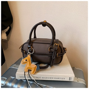 Detaillierte Nahaufnahme der dunkelbraunen Mini-Boston-Tasche mit Kontrastnähten und Anhänger