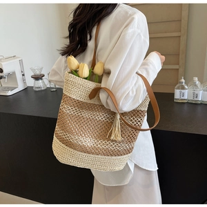Detail of straw woven tote bag with fringe tassel and leather strap in a cafe setting