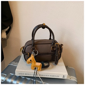 Detailansicht der dunkelbraunen Boston Bag aus Leder mit Kontrastnähten und gelbem Anhänger