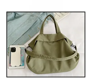 Vue à plat d'un sac fourre-tout en nylon vert armée sur draps blancs avec accessoires