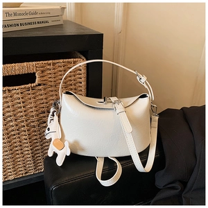 Close-up of stylish white crescent handbag with PU leather texture and rabbit charm on a table