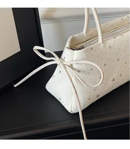 Detail view of cream star-print baguette bag with delicate side ribbon bow and zipper