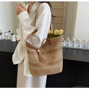 Close-up of woven straw tote bag featuring leather handles and tassel wood bead detail