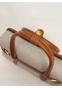 Dettaglio del manico in pelle marrone con anello dorato e cuciture su una borsa strutturata