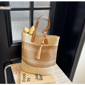 Detail of striped straw tote bag with brown leather handles and decorative tassel