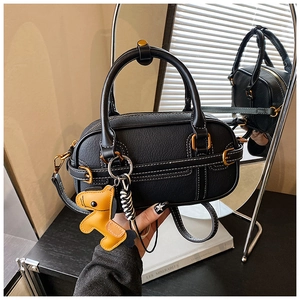 Detail der schwarzen Boston-Tasche mit weißen Nähten, Lederpony-Anhänger und Goldbeschlägen