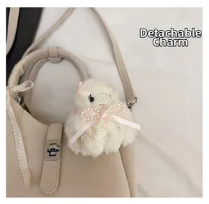 Gros plan sur un bijou de sac mouton en peluche blanc avec ruban rose sur sac en cuir