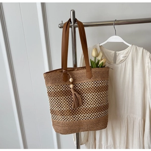 Close-up of woven straw tote bag with long tassels, wooden beads and leather shoulder strap