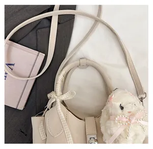 Détail d'un sac seau beige avec poignée ronde, nœud à carreaux et pendentif lapin perlé