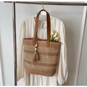 Detail of hollow woven straw tote bag with brown leather handles and tassel pendant decoration