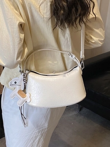 Minimalist cream shoulder bag with horse pendant shown on a model in a warm indoor setting