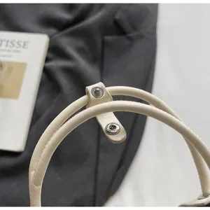 Détail des poignées cylindriques avec boutons-pression en métal argenté sur sac seau blanc
