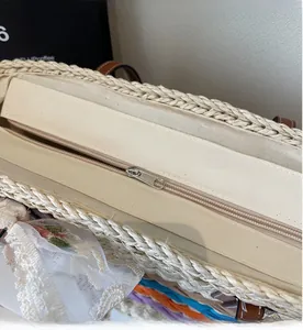 Detailed view of the smooth metal zipper and lace trim on a woven straw tote bag