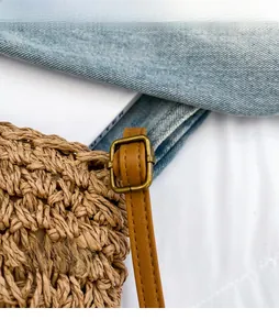 Detail view of straw shoulder bag showing the adjustable faux leather strap and bronze buckle