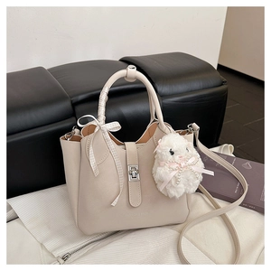 Détail d'un sac à main beige avec fermoir argenté, ruban et pendentif lapin en peluche